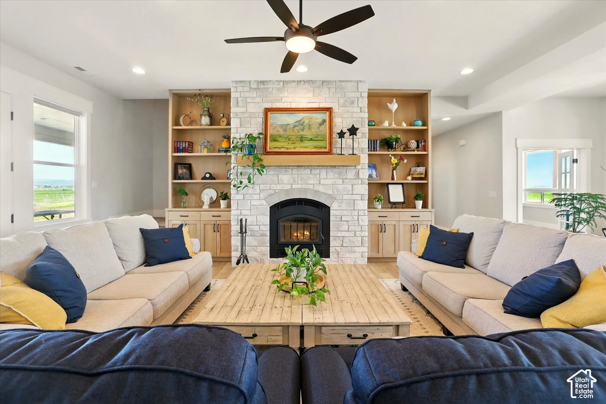 Stone-faced fireplace with a wood-finish mantel, custom floor-to-ceiling built-in cabinetry, recessed lighting, and an integrated ceiling fan