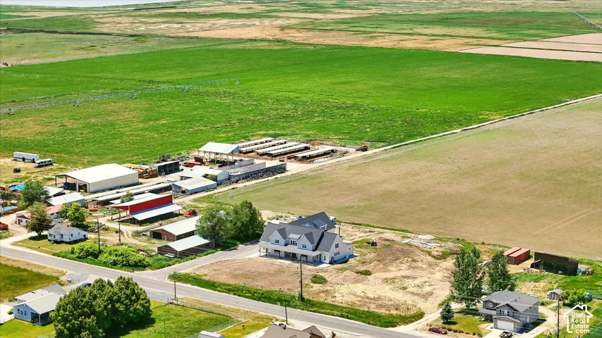Aerial perspective featuring extensive acreage, multiple agricultural outbuildings, covered livestock pens, and a multi-level residence with a gabled roofline