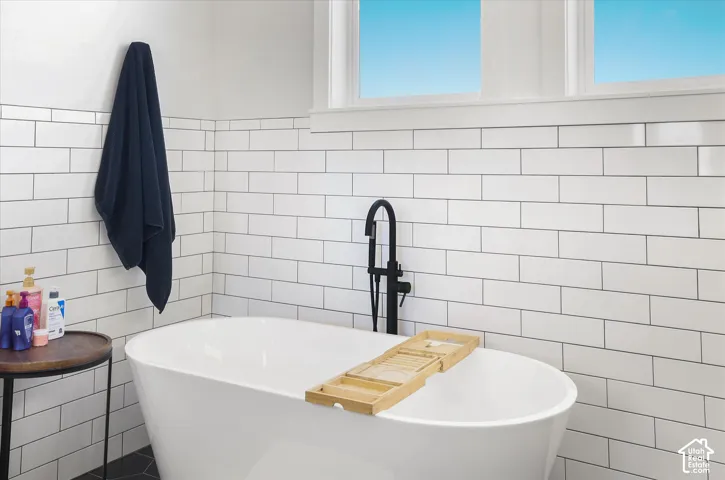 Freestanding soaking tub featuring a matte black floor-mounted faucet and white subway tile wall surround