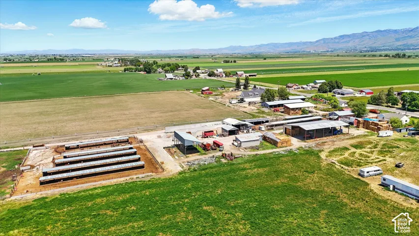 Aerial perspective of expansive acreage featuring multiple agricultural outbuildings, covered livestock pens, established fencing, and mountain scenery