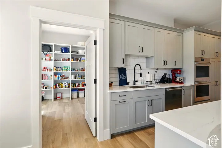Prep Kitchen featuring shaker-style cabinetry, white subway tile backsplash, light-toned stone countertops, built-in double oven, and a walk-in pantry with floor-to-ceiling shelving