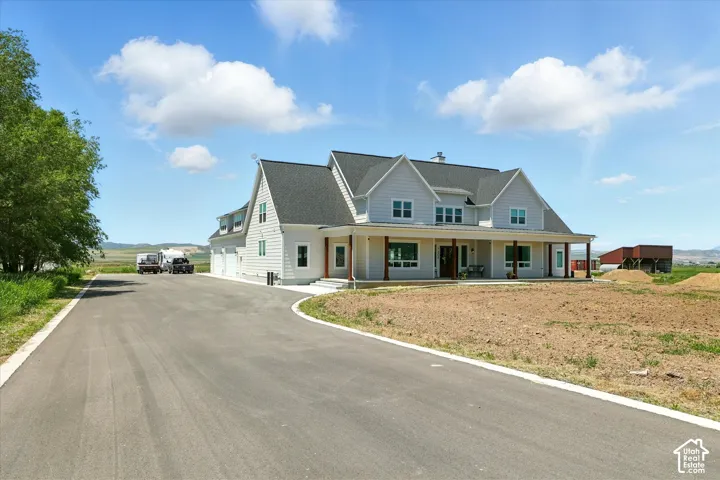 Two-story residence featuring light-toned horizontal siding, a multi-gabled asphalt shingle roof, a covered front porch with timber support columns, and an expansive asphalt driveway