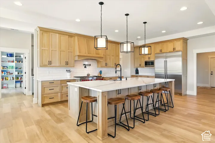 Kitchen featuring natural wood cabinetry, central island with quartz countertop, stainless steel appliances, subway tile backsplash, and three geometric pendant lights