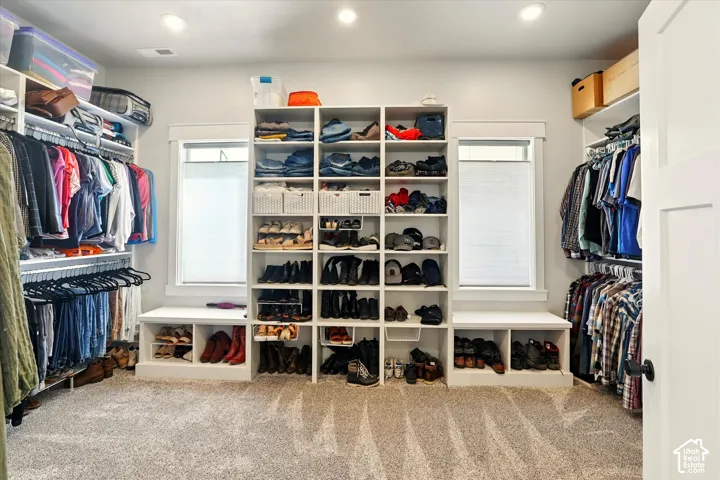 Custom walk-in closet featuring floor-to-ceiling built-in shelving, integrated lower storage benches, dual windows with casing, recessed lighting, and carpeted flooring