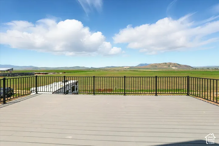 Spacious elevated deck featuring composite decking, black metal balusters, and expansive mountainous and open-field scenery