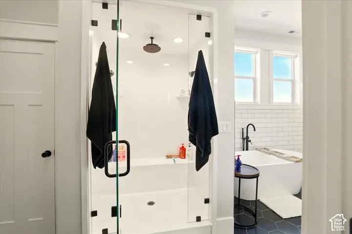 Walk-in shower featuring a glass enclosure with matte black hardware, integrated bench seat, and ceiling-mounted rainfall showerhead, plus two additional shower heads,  paired with a freestanding soaking tub with matte black floor-mounted faucet and subwa