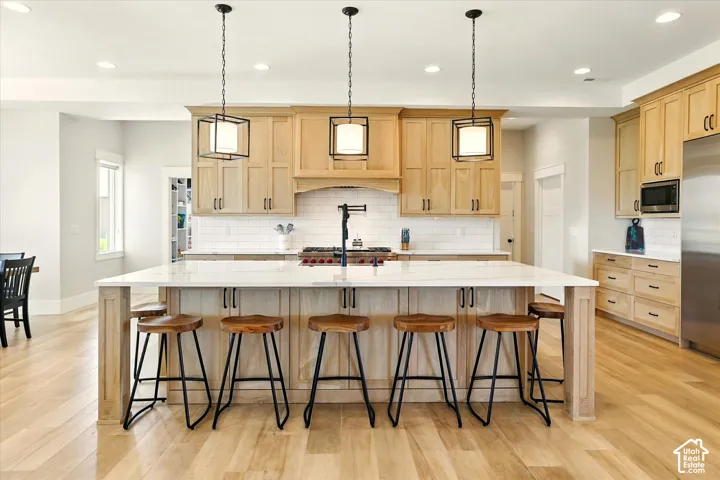 Kitchen featuring white oak cabinetry, quartz countertops, a central island with matte black fixtures, tile backsplash, and recessed lighting