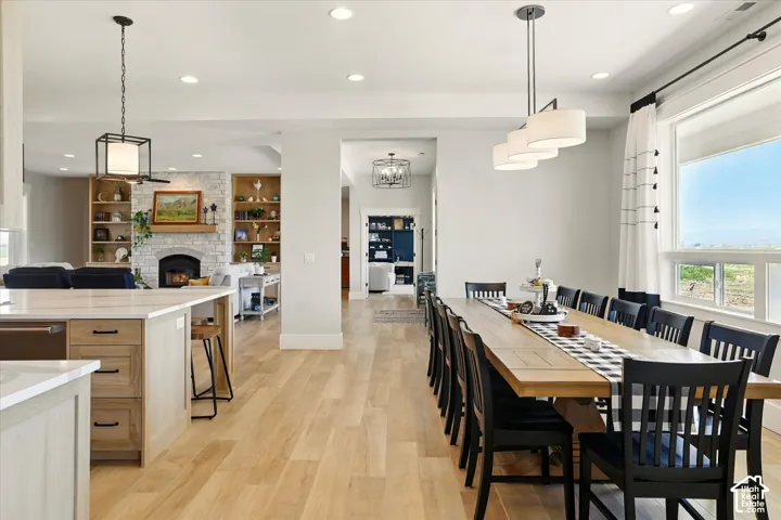 Open-concept space featuring light wood-finish tile flooring, recessed lighting, a stone-faced fireplace with built-in shelving, a kitchen island with stone countertops, and tiered pendant lighting