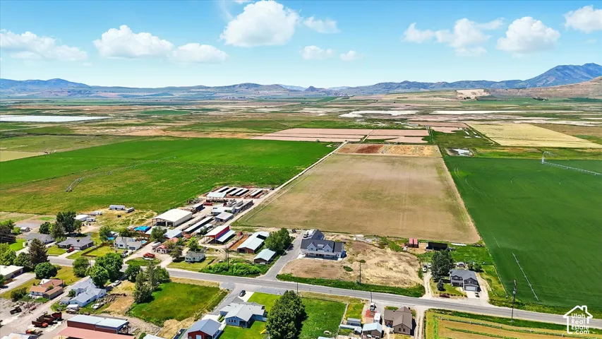 Aerial perspective of expansive agricultural acreage featuring multiple outbuildings, large-scale grazing areas, road access, and prominent mountain backdrops