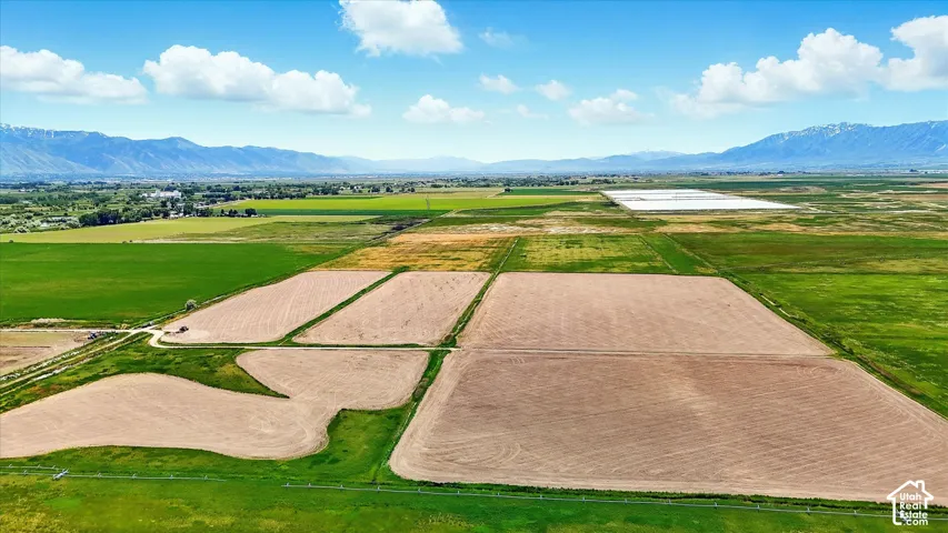 Expansive acreage featuring cleared soil plots, open green space, and mountain range backdrop