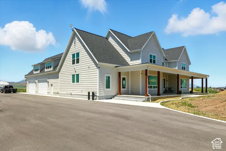 Multi-gabled exterior featuring horizontal lap siding, a wrap-around porch with stained wood columns, multiple dormer windows, and an attached multi-car garage (oversized 4+ car)