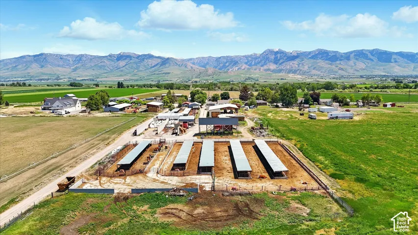 Extensive agricultural parcel featuring multi-bay covered livestock structures, fenced enclosures, open pasture, and mountain range backdrop