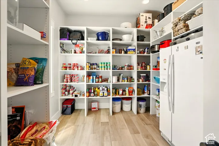 Walk-in pantry featuring white floor-to-ceiling custom shelving, wood-finish tile flooring, and a dedicated space for a side-by-side refrigerator