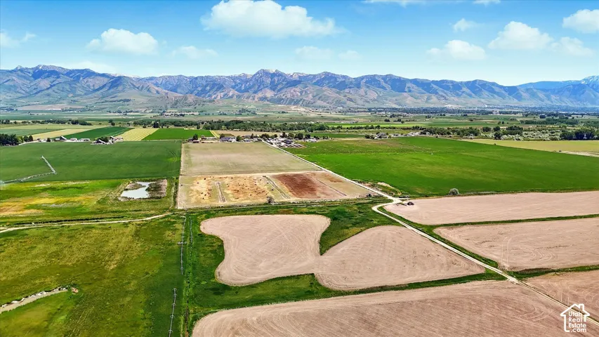 Expansive acreage featuring cleared agricultural land, irrigation pond, and mountain range scenery