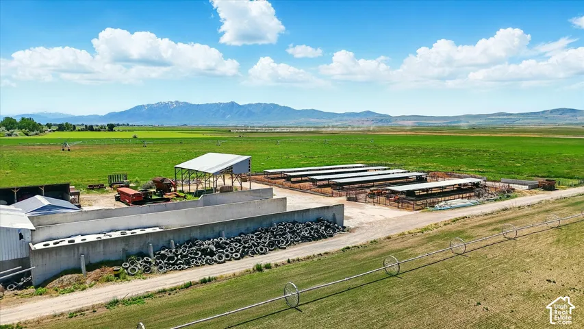 Expansive acreage featuring irrigated fields, mountain backdrop, open-air agricultural shelters, and concrete livestock containment structures