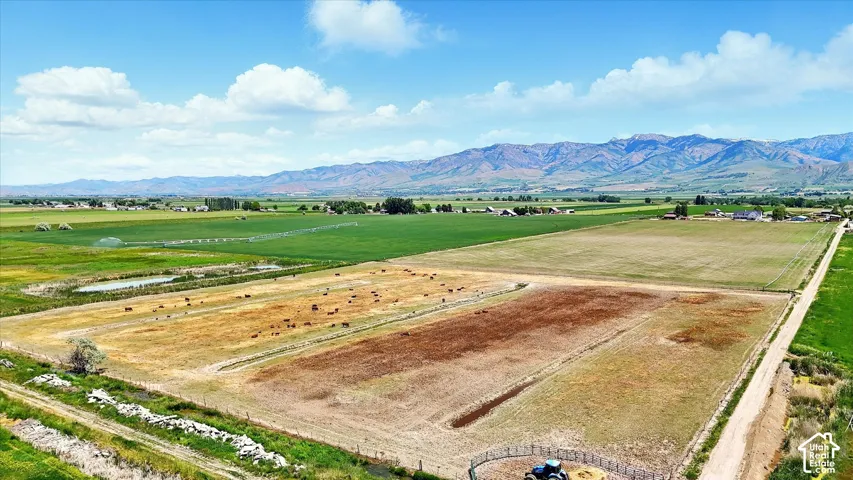 Expansive agricultural acreage featuring fenced pastures, a natural pond, dirt access roads, and mountain backdrop