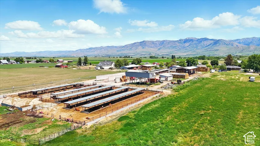 Expansive agricultural property featuring multiple covered livestock shelters, fenced paddocks, auxiliary outbuildings, and mountain range scenery