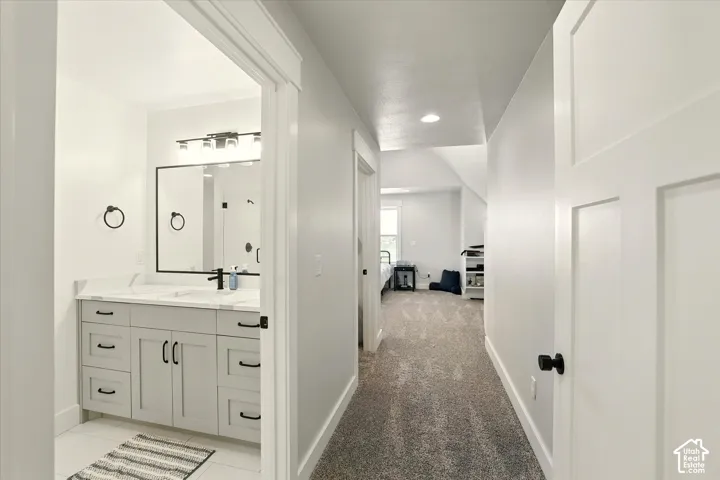 Entry into 2nd suite with hallway to bathroom, walk-in closet & bedroom. Bathroom vanity featuring light-toned cabinetry, undermount sink, and a stone-surface countertop, accented by a black-framed mirror and matching hardware