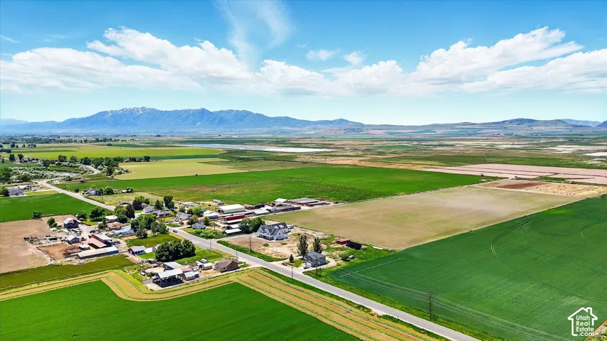 Aerial perspective featuring expansive agricultural acreage, paved road frontage, and prominent mountain backdrops