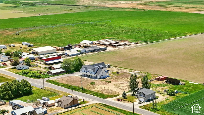 Aerial perspective of a sprawling rural acreage featuring extensive pasture land, multiple agricultural structures, and a residential dwelling with a covered porch