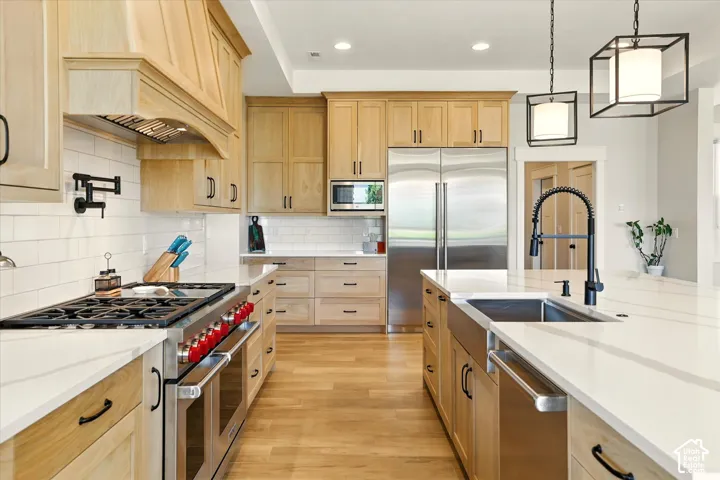 Kitchen featuring light-finish cabinetry, white countertops, a professional-style stainless steel Wolf gas range, a farmhouse sink with a matte black faucet, and pendant lighting