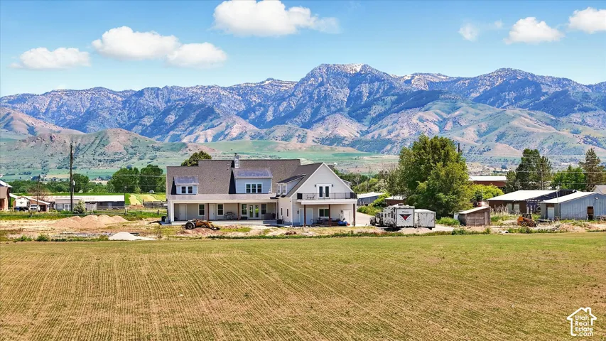 Multi-level exterior featuring light-toned siding, a shingled roof, a ground-level covered patio, an upper-level balcony, and expansive mountain scenery