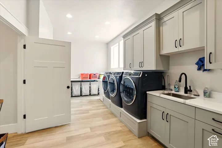 Laundry area featuring shaker-style cabinetry, white solid-surface countertops, an undermount sink with matte black hardware, and wood-finish flooring