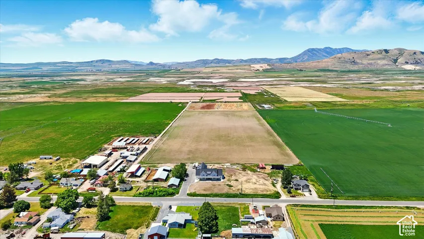 Aerial perspective of expansive acreage featuring irrigated agricultural fields, multiple outbuildings, a residential structure, and a mountainous backdrop