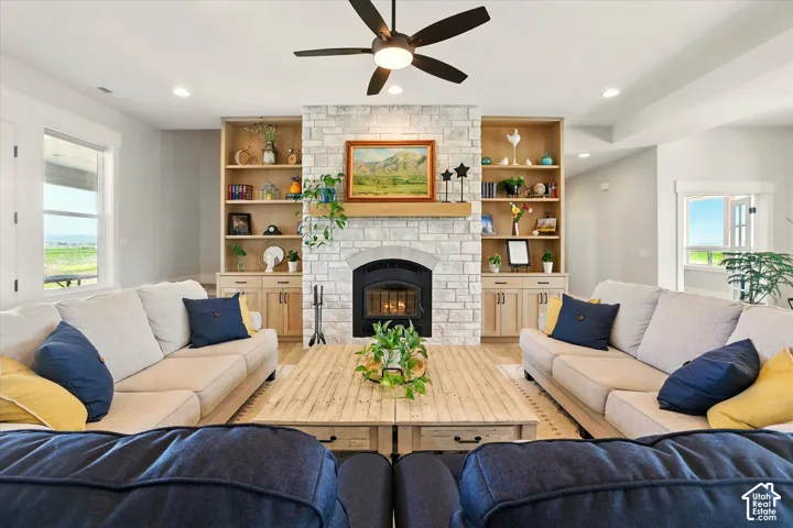 Stone-faced fireplace with a wood-finish mantel, custom floor-to-ceiling built-in cabinetry, recessed lighting, and an integrated ceiling fan