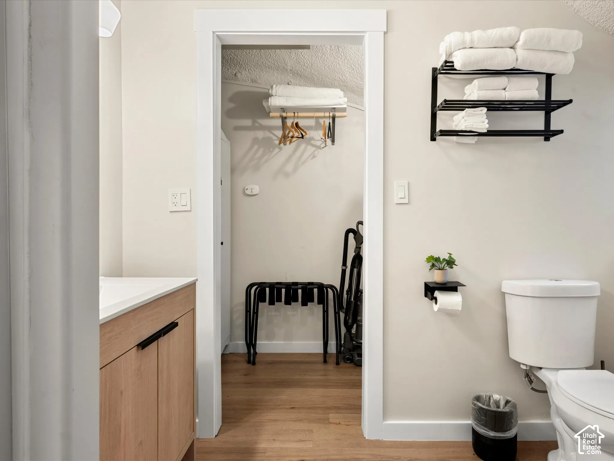 Wood-finish flooring, vanity with a white countertop, and black matte metal wall-mounted shelving
