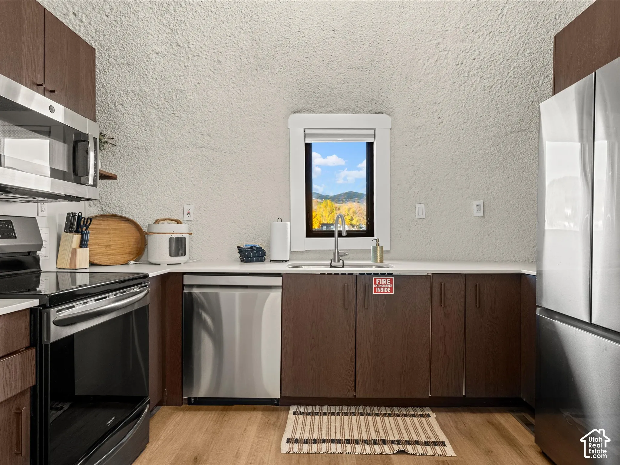 Kitchen featuring dark wood-finish cabinetry, solid-surface countertops, stainless steel appliances, and wood-finish flooring