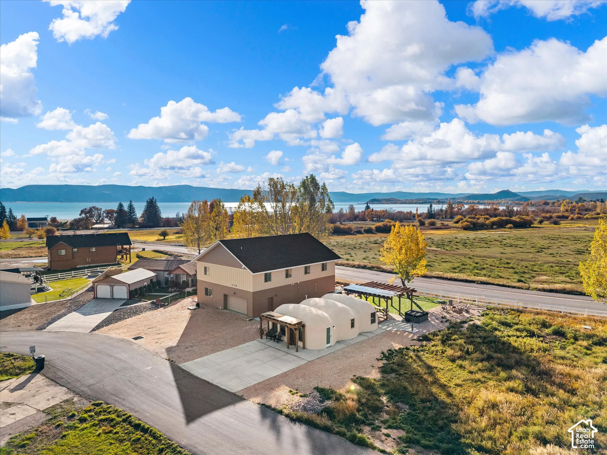 Aerial perspective of a multi-structure property featuring a two-story residence, a multi-domed architectural addition, concrete parking areas, and timber-framed pergola structures