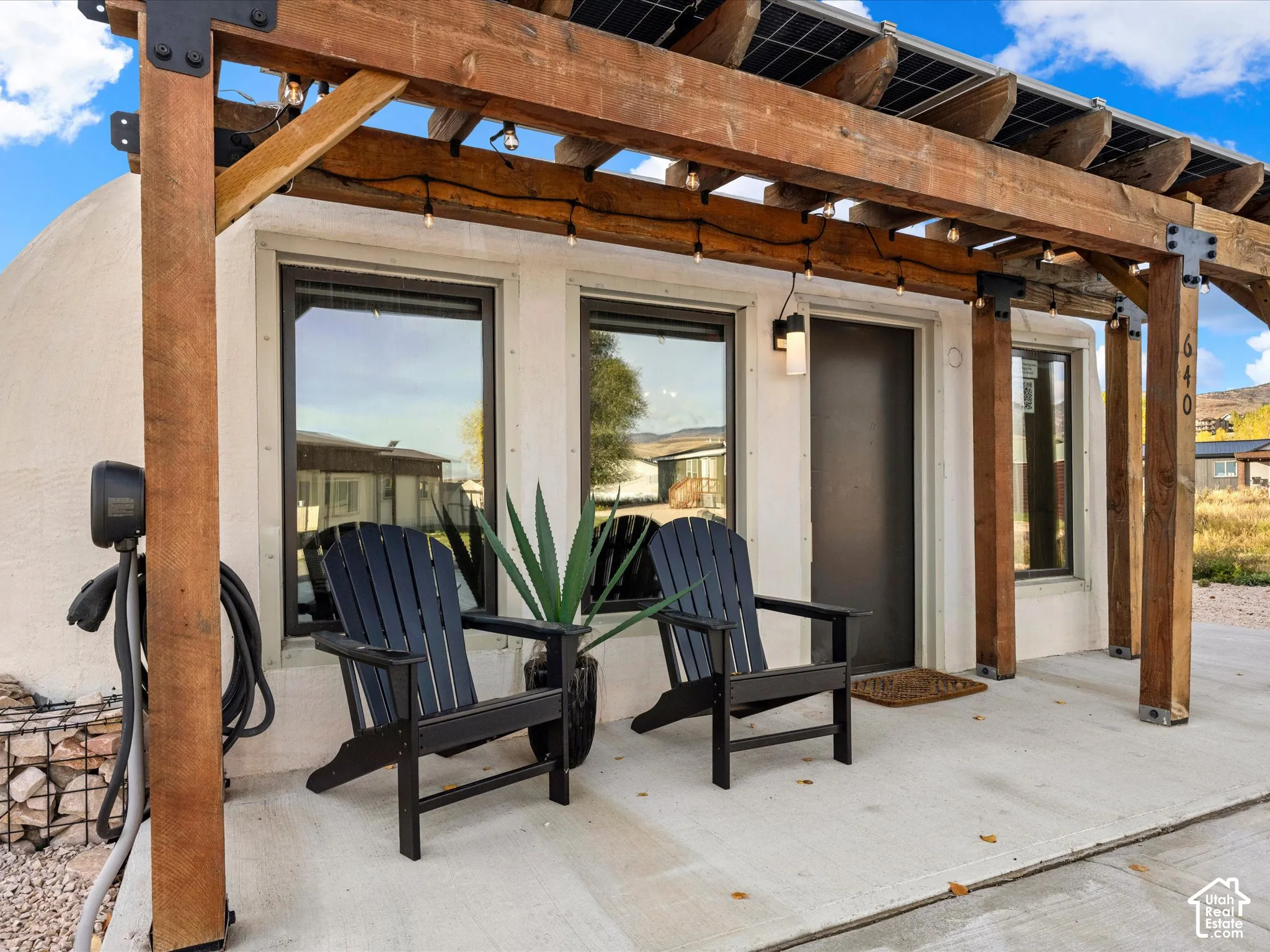 Exterior featuring a timber-frame pergola, integrated solar panels, concrete porch, and electric vehicle charging station