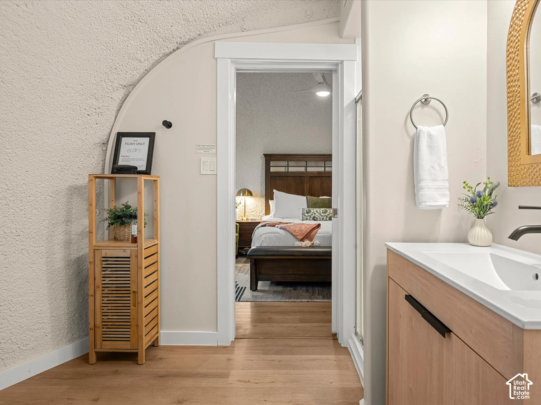 Curved architectural wall featuring a textured finish, wood-finish flooring, vanity with a white countertop, and a wall-mounted matte black faucet