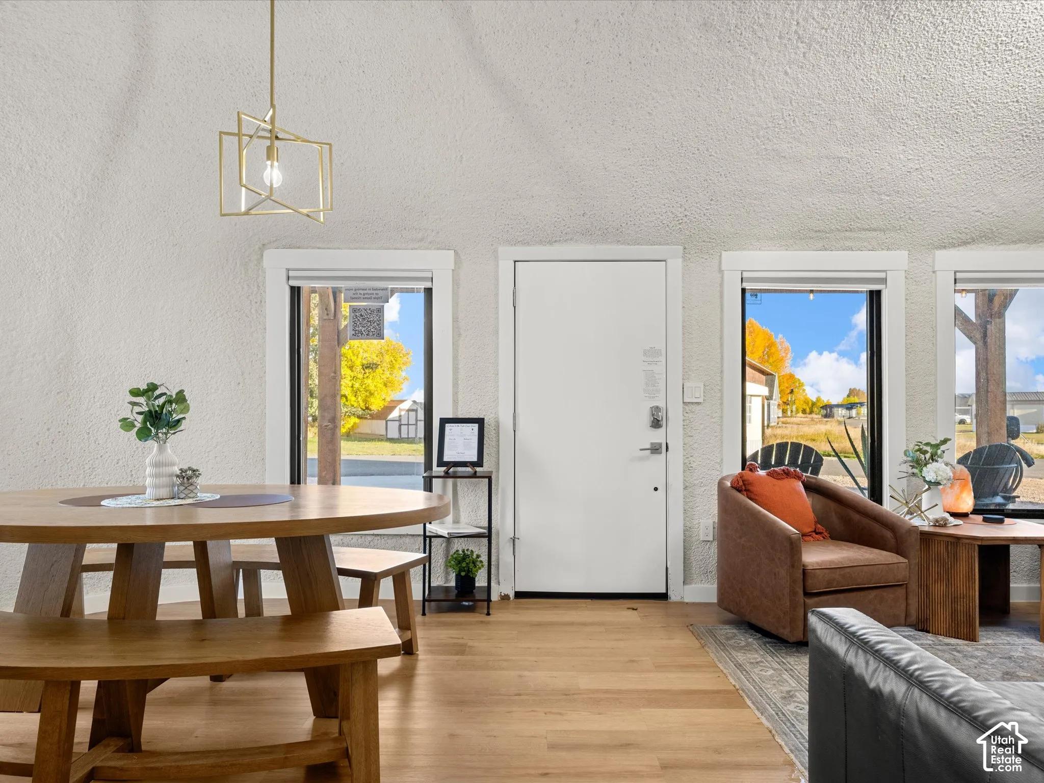 Vaulted, textured ceiling featuring a geometric metal pendant light, wood-finish flooring, and multiple large windows with white trim