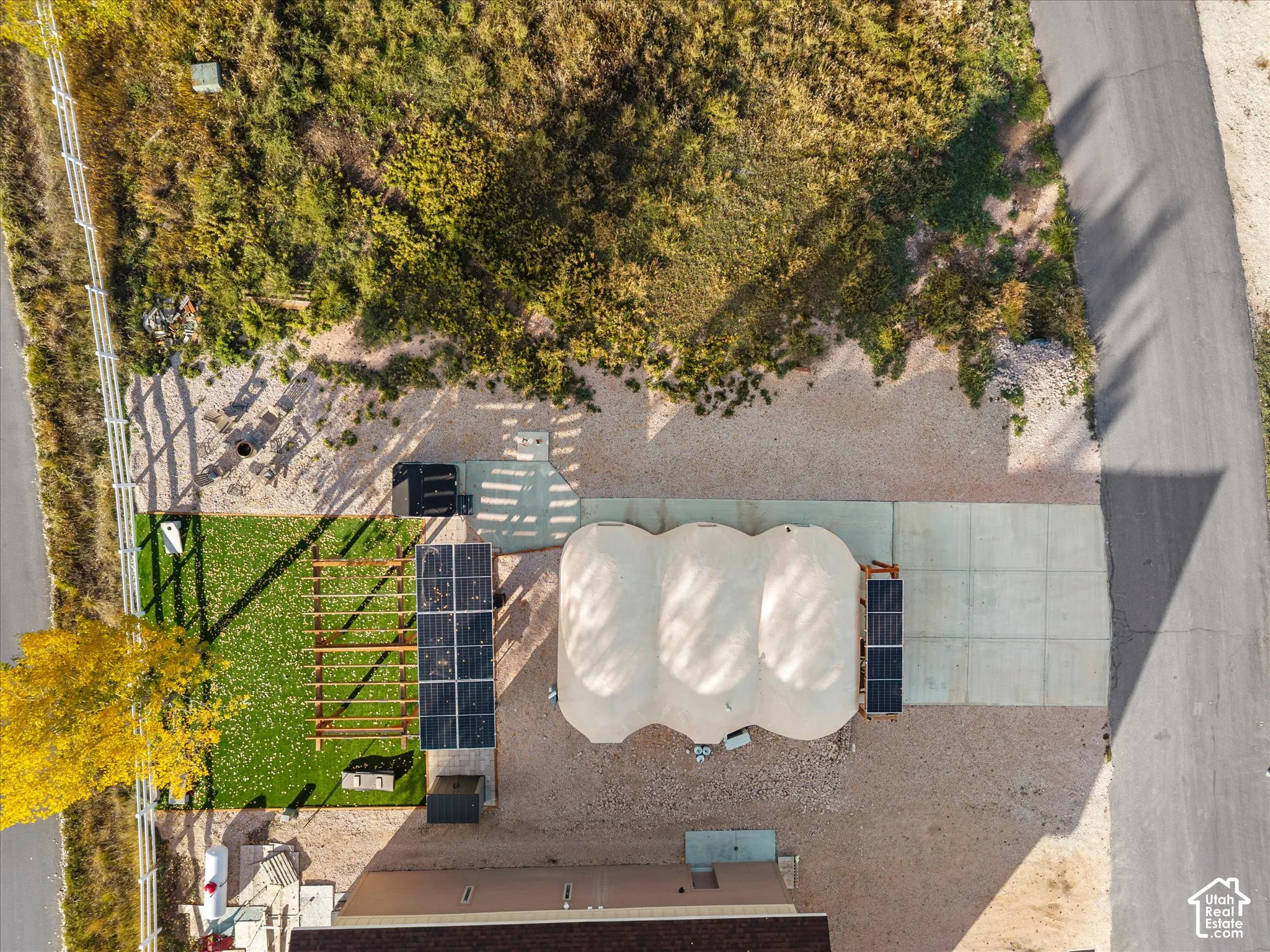 Aerial view of grounds featuring a triple-dome structure, solar panel arrays, a wooden pergola, a paved concrete pad, and white perimeter fencing