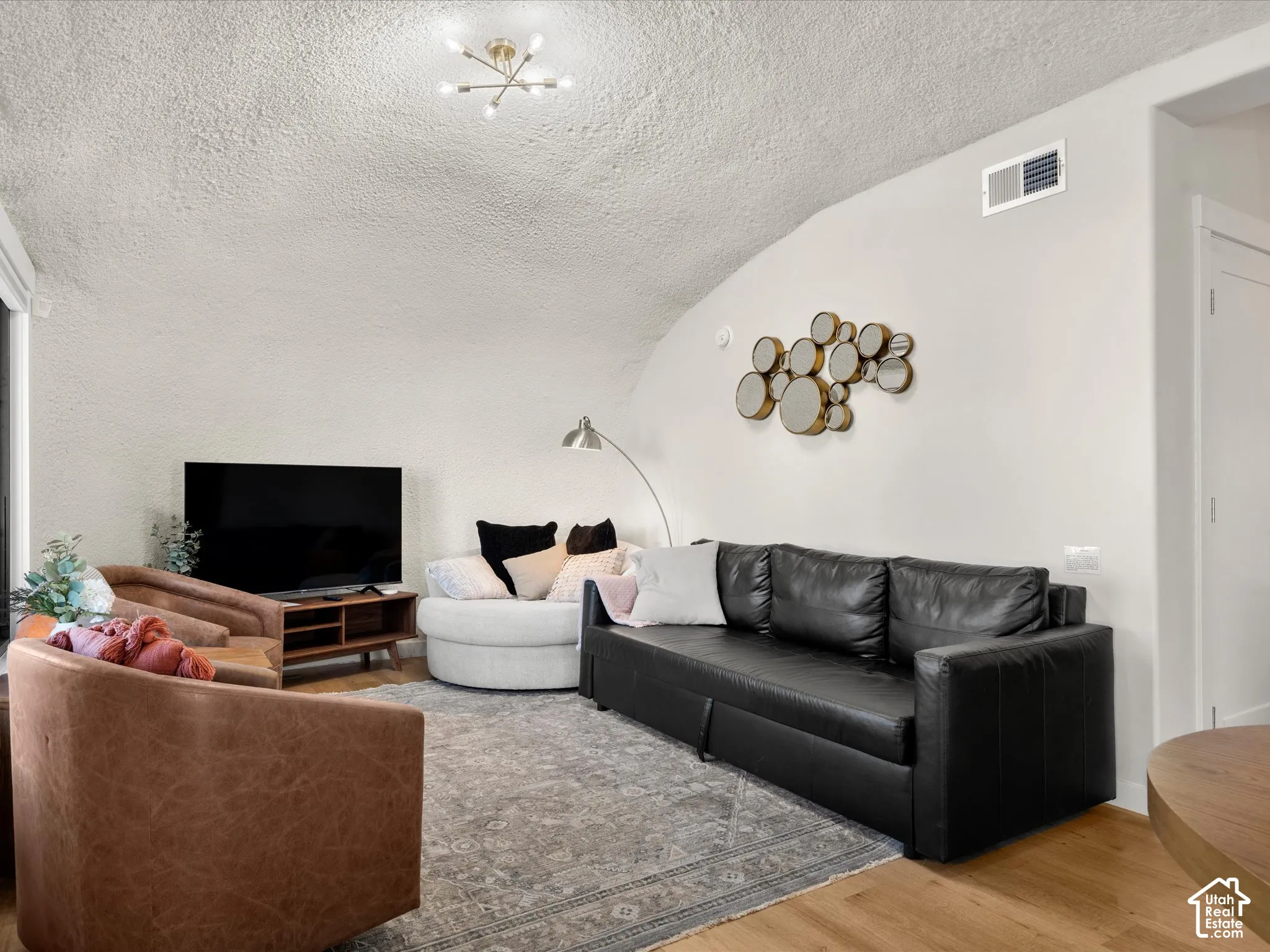Vaulted ceiling, wood-finish flooring, and multi-arm brass-finish ceiling light fixture