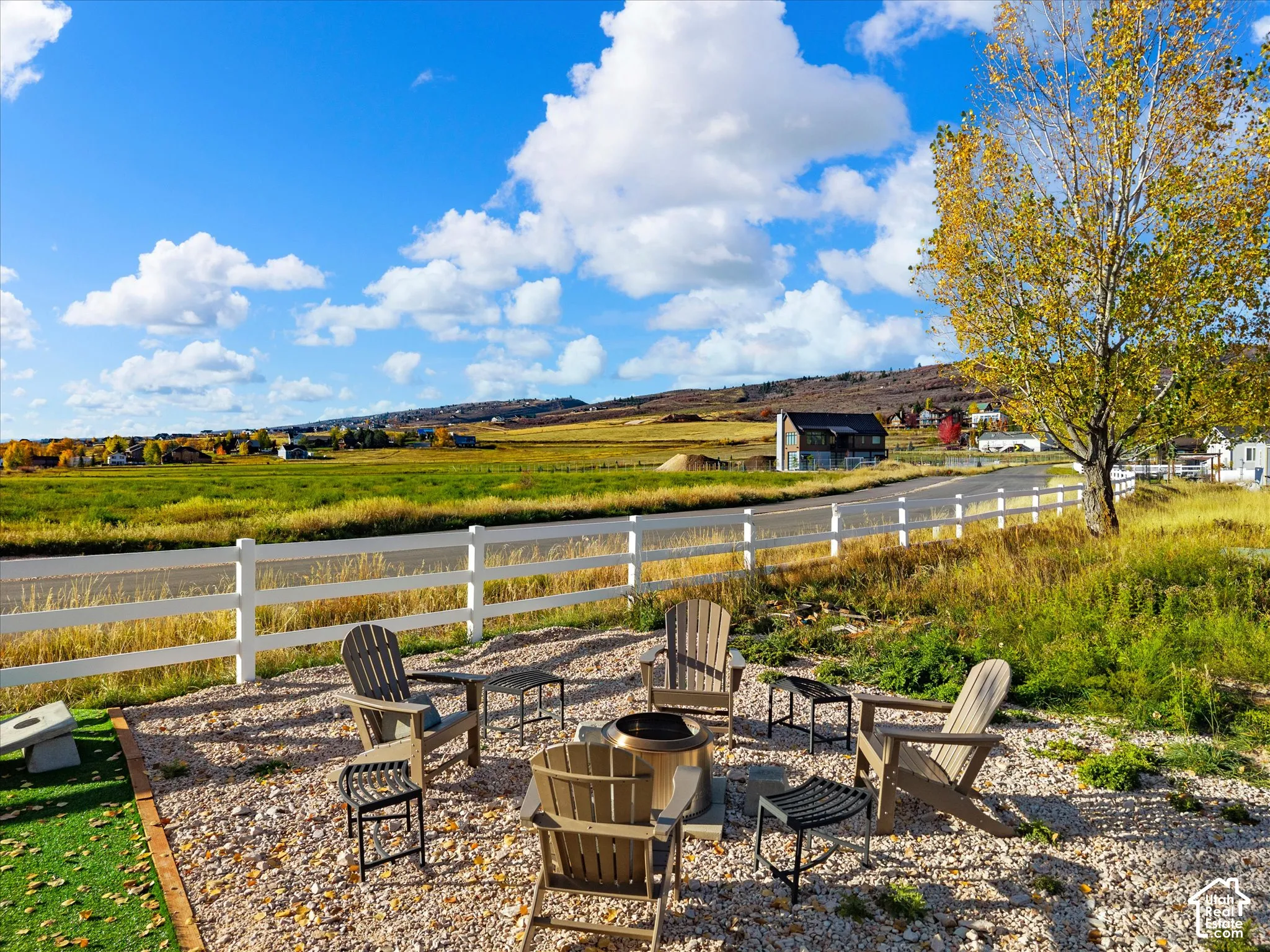 Gravel patio featuring a built-in metal fire pit, enclosed by white vinyl fencing with surrounding open space and mountain horizon