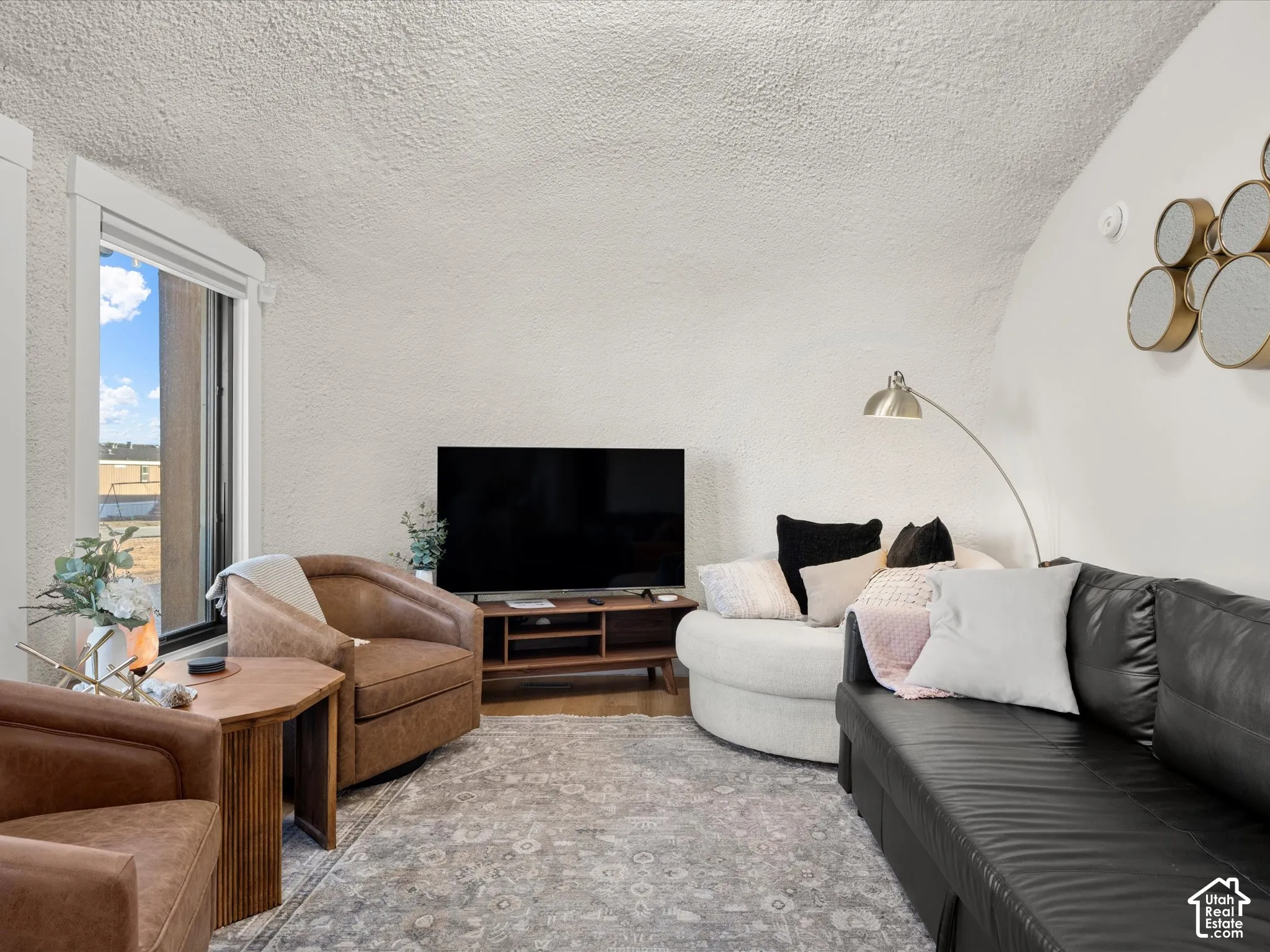 Vaulted ceiling featuring a textured finish, wood-finish flooring, and a large window