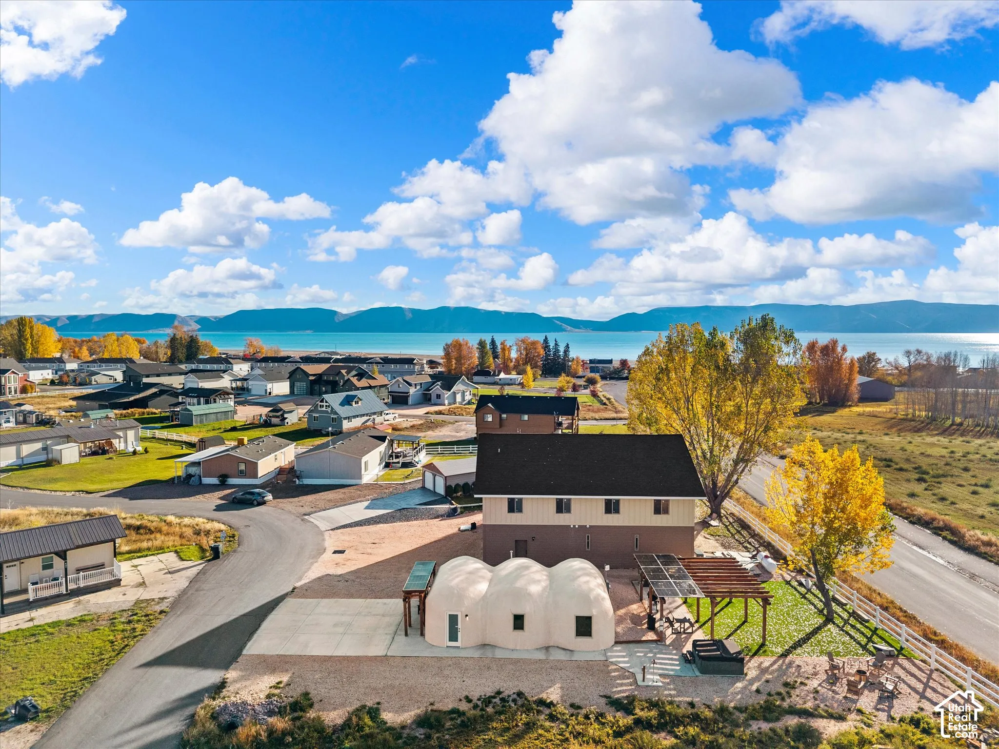 Multi-domed architectural structure featuring a two-story addition, a pergola-covered patio, and a concrete driveway, set against a backdrop of mountains and water