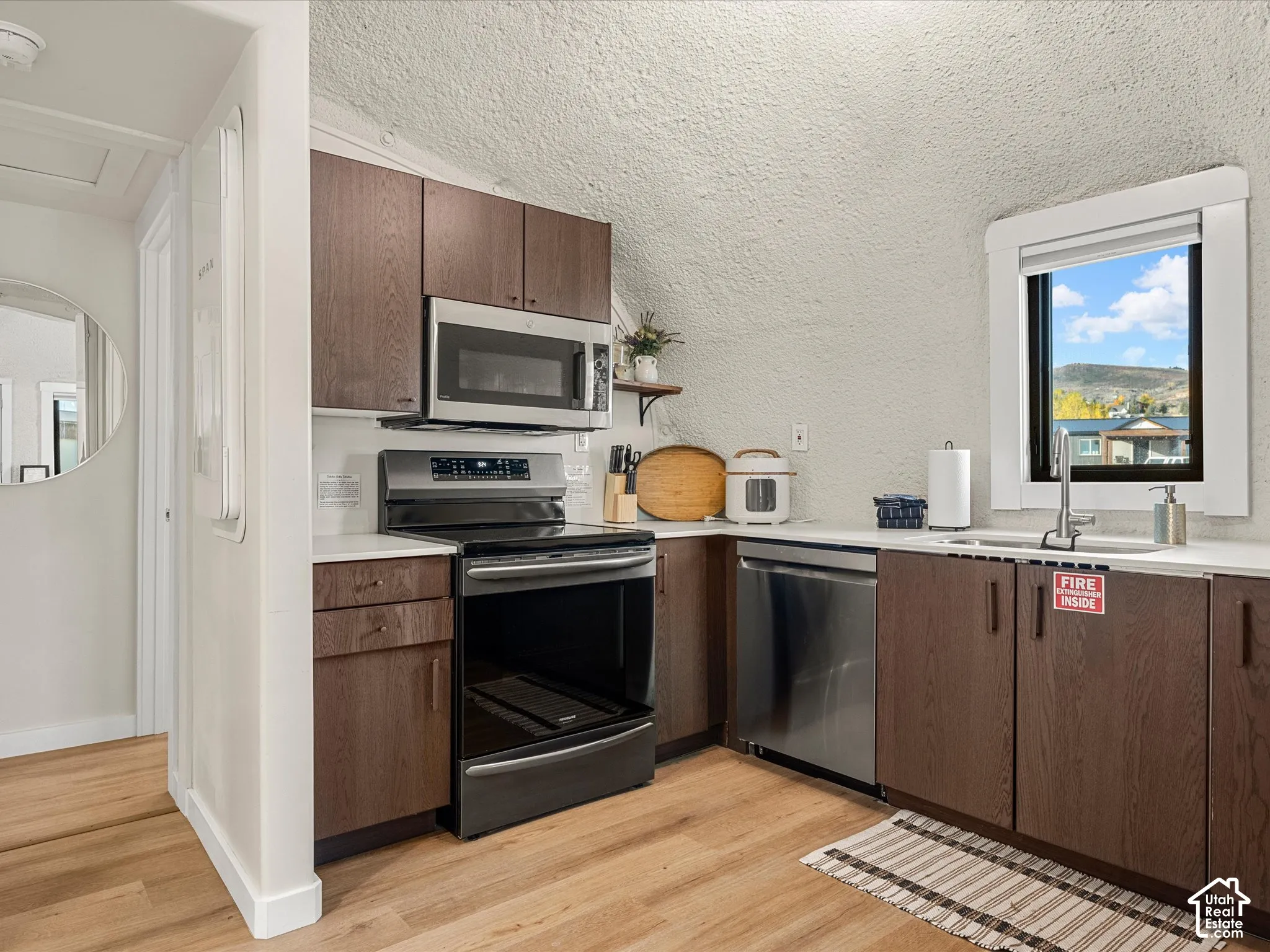 Kitchen featuring dark wood-finish cabinetry, stainless steel appliances, solid surface countertops, and light-toned wood-finish flooring