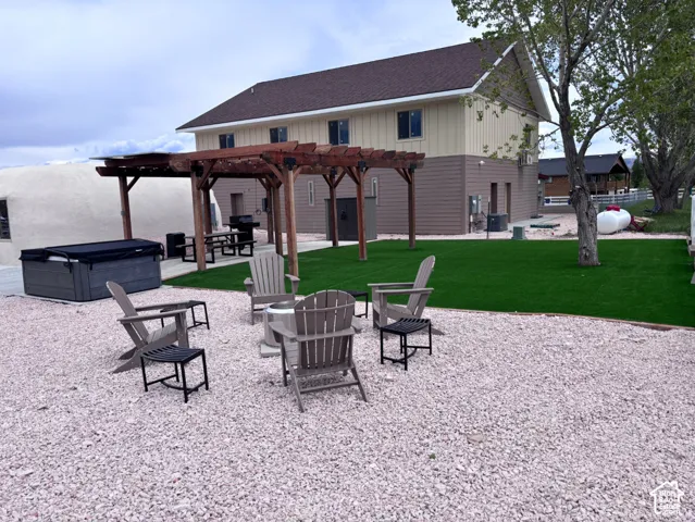 Outdoor living area featuring a wooden pergola, synthetic lawn, gravel grounds, and a built-in hot tub