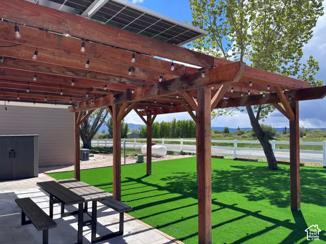 Timber pergola structure featuring integrated string lighting, solar panel roof array, and synthetic turf lawn bordered by white rail fencing