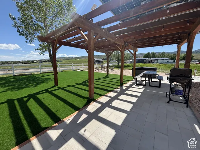 Outdoor living space featuring a timber pergola, paved patio, synthetic turf lawn, and perimeter white rail fencing