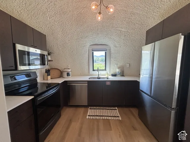 Kitchen featuring dark cabinetry, solid-surface countertops, stainless steel appliances, a central window, and wood-finish flooring