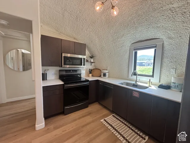 Kitchen featuring dark wood-finish cabinetry, white solid-surface countertops, stainless steel appliances, wood-finish flooring, and a vaulted textured ceiling