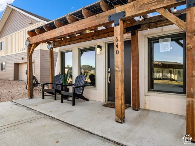 Entryway featuring a concrete porch, a timber-frame pergola with integrated solar panels, and large-format windows with dark frames