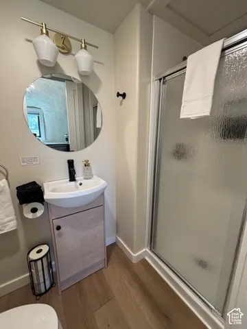 Bathroom featuring wood-finish vanity, circular wall-mounted mirror, matte black faucet, gold-tone dual-light fixture with glass shades, and enclosed shower with textured glass door