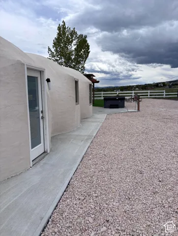 Monolithic dome structure featuring a smooth stucco exterior, concrete walkway, and gravel surfacing, complemented by an integrated hot tub and perimeter white rail fencing