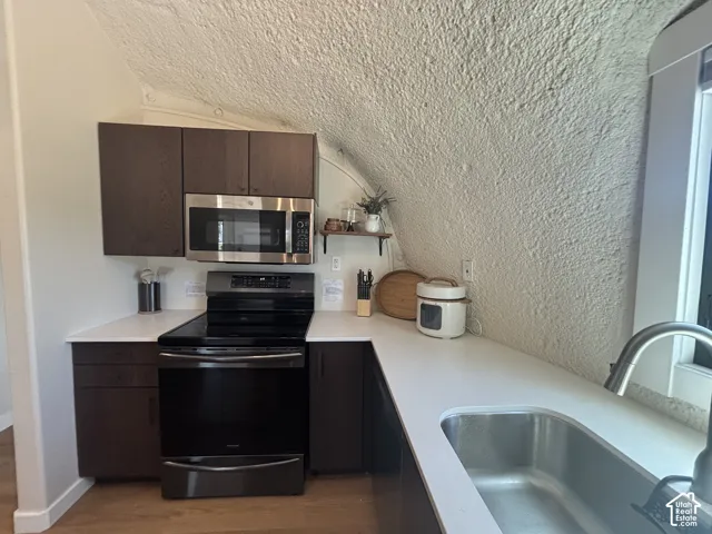 Kitchen featuring dark wood-finish cabinetry, solid surface countertops, stainless steel microwave, black electric range, and stainless steel undermount sink with a gooseneck faucet